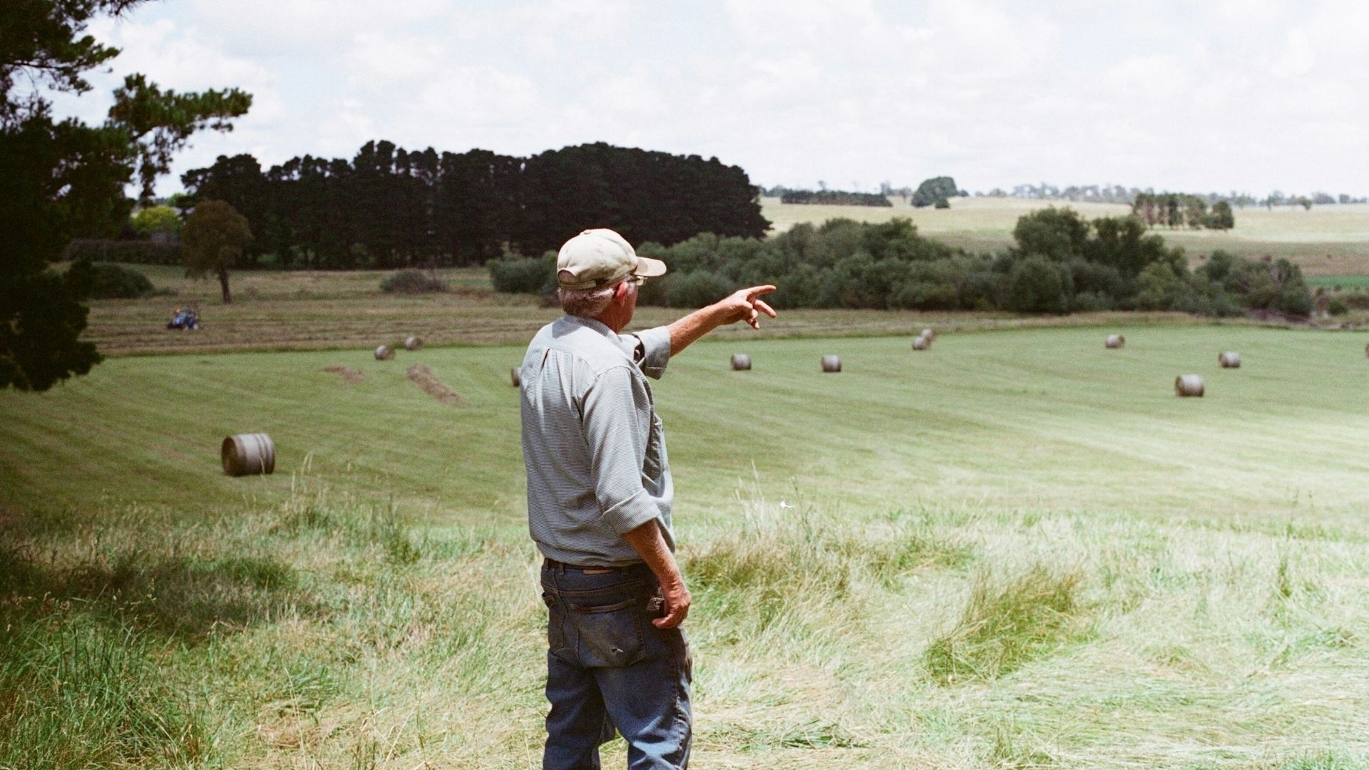 Person overlooking rural farmland with hay bales scattered across open fields.