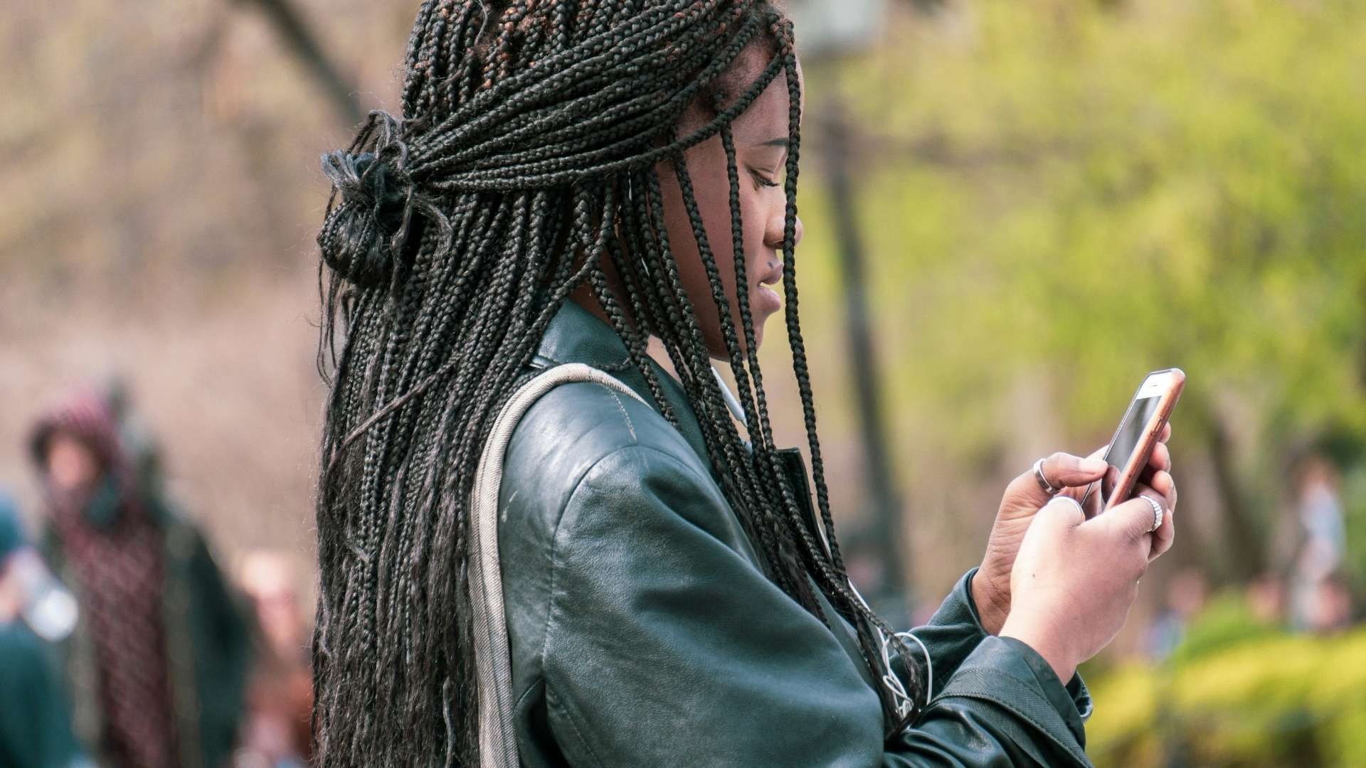Person using a smartphone outdoors with blurred greenery in the background