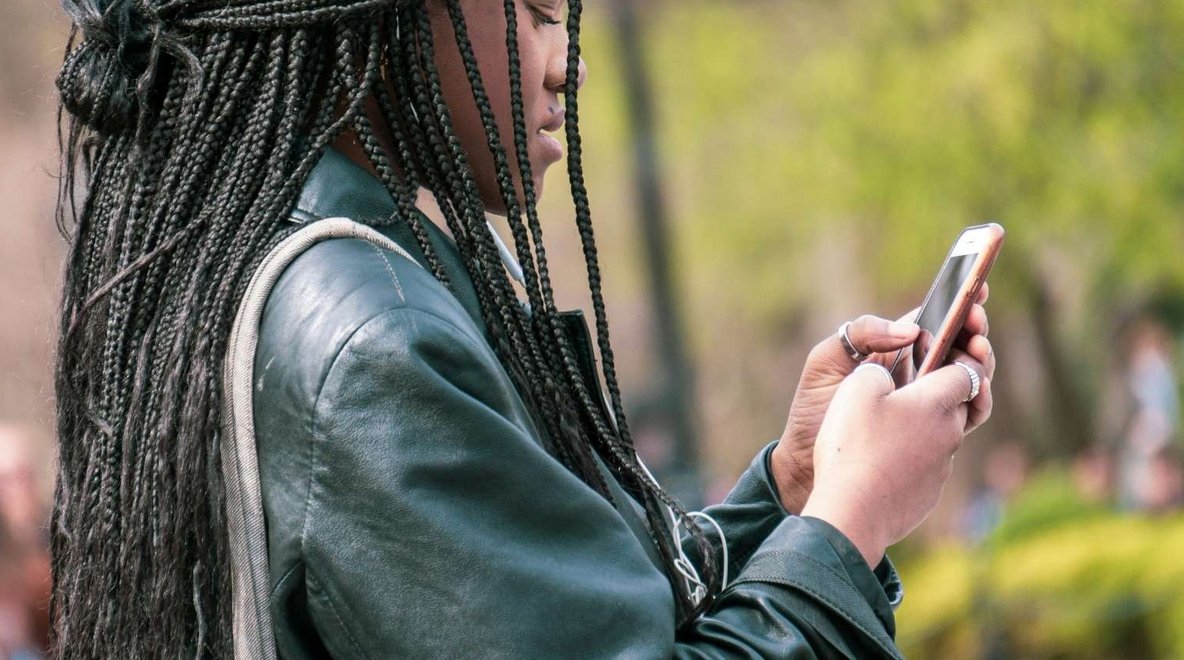 Person using a smartphone outdoors with blurred greenery in the background