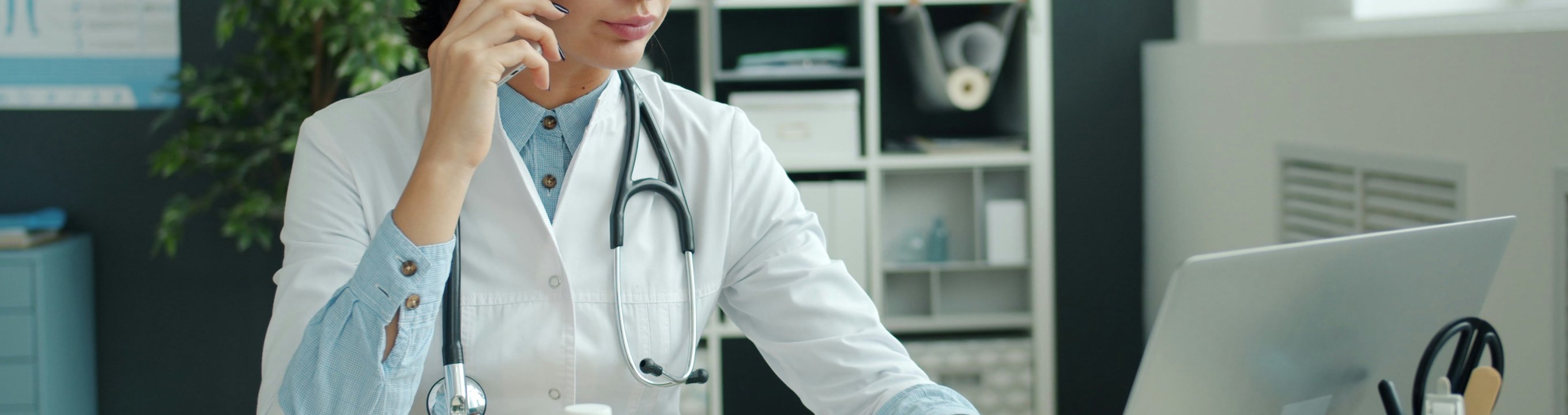 Doctor using a phone while working on a laptop at a desk