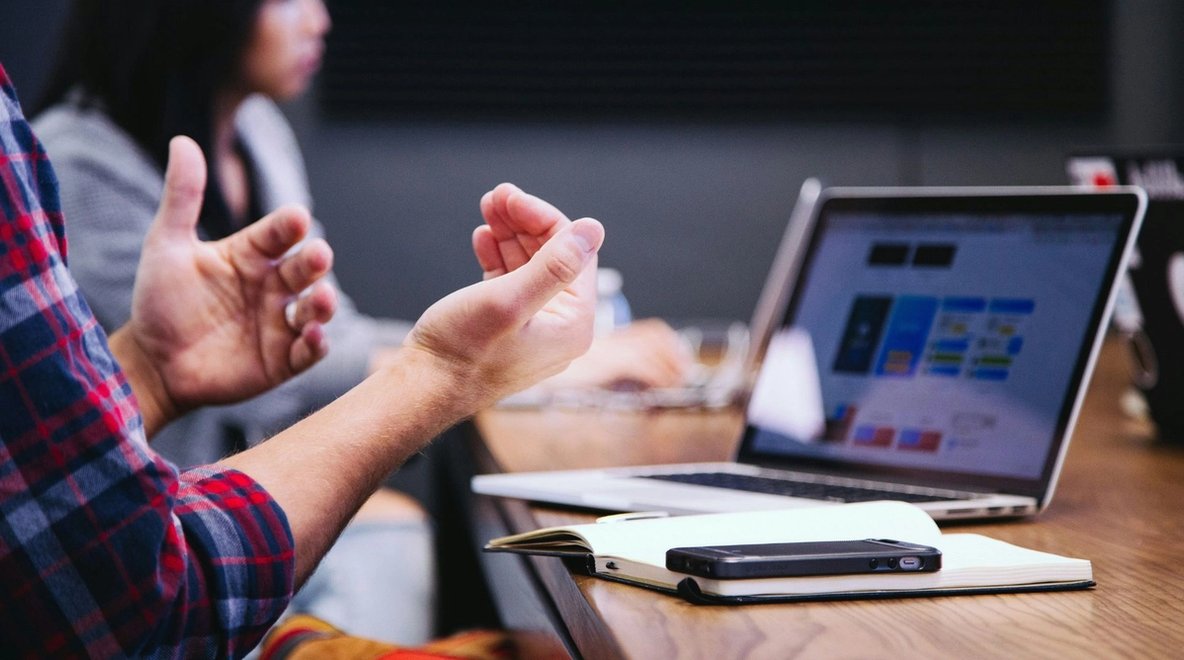 People sitting at a table with a laptop and phone, with one person gesturing during discussion.