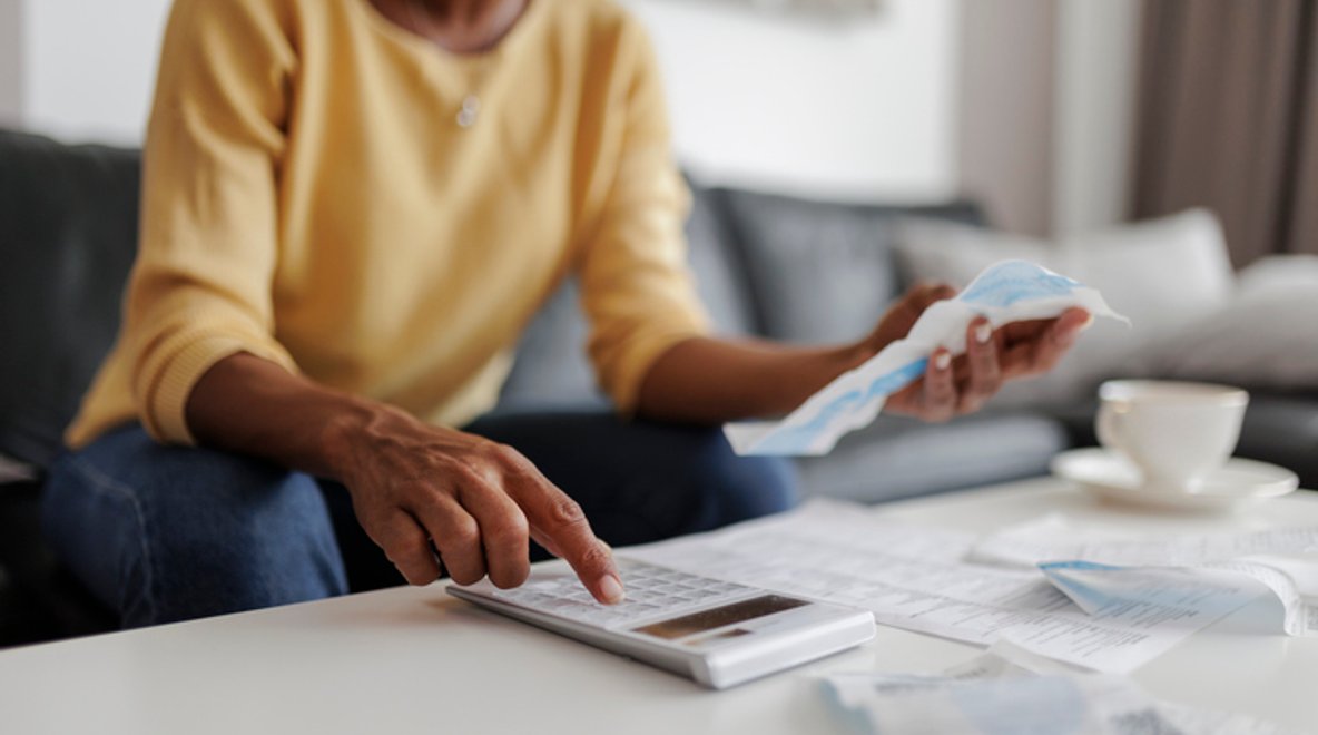 Person using a calculator and reviewing bills at a table.
