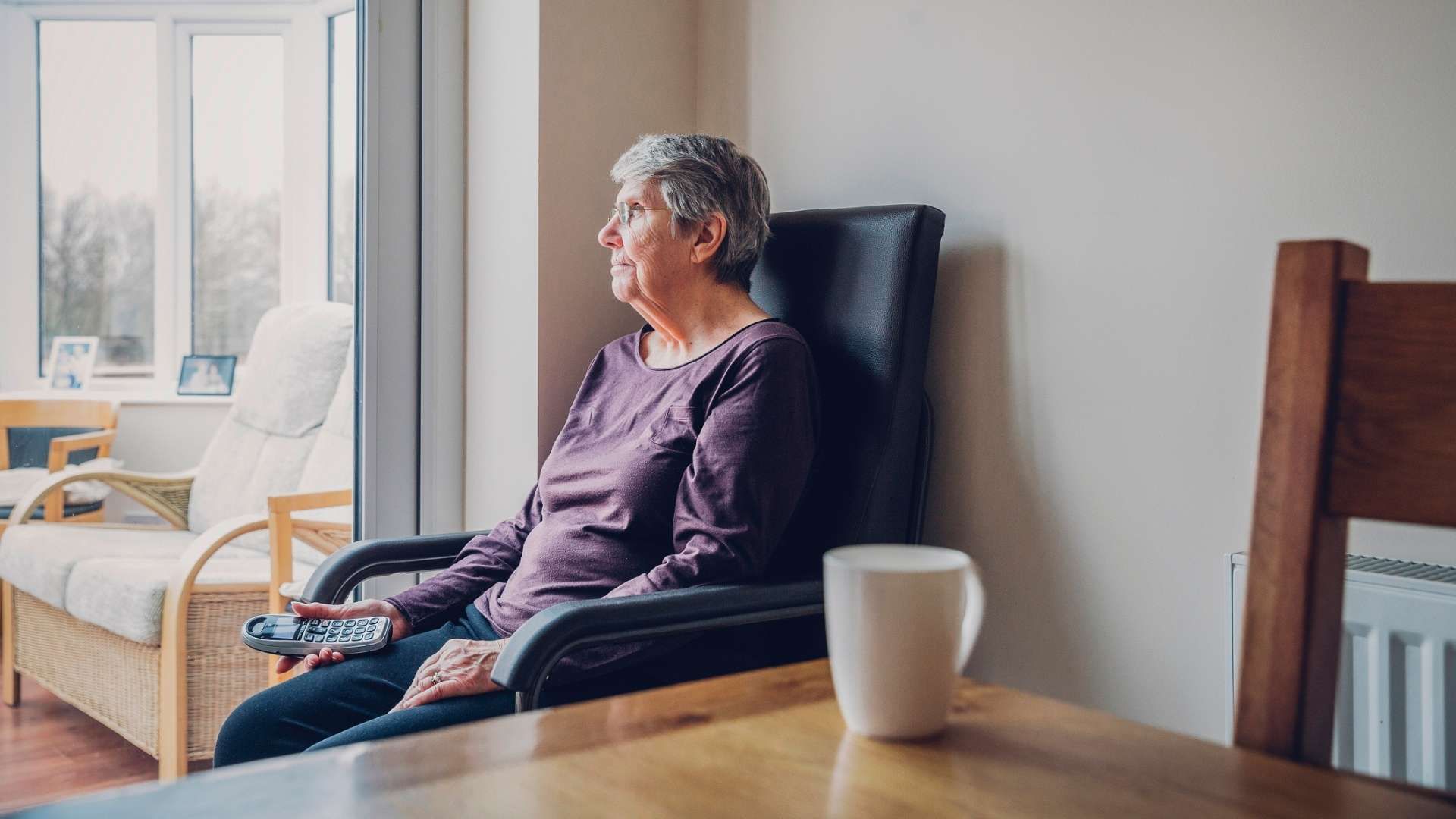 Person sitting in a chair by a window holding a telephone.