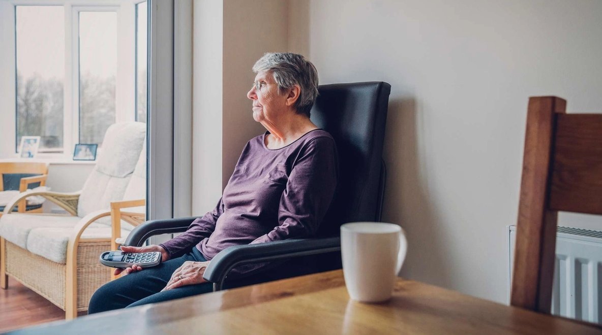 Person sitting in a chair by a window holding a telephone.