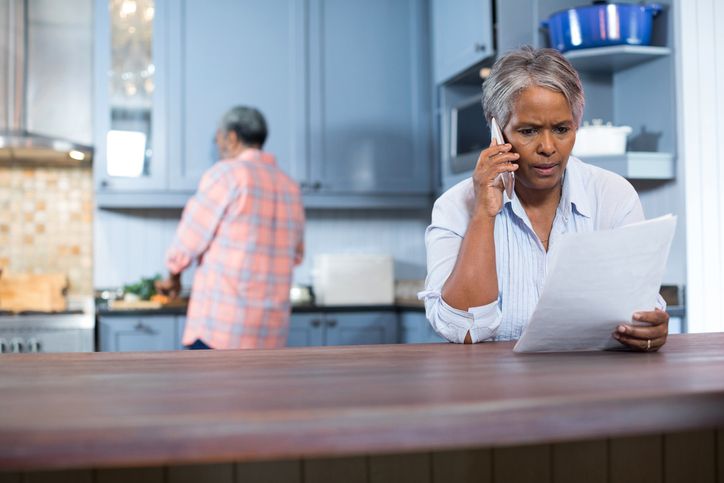 Person sitting at a table holding a document while talking on a smartphone.