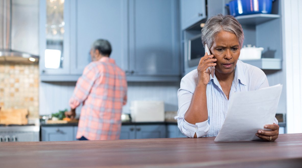 Person sitting at a table holding a document while talking on a smartphone.