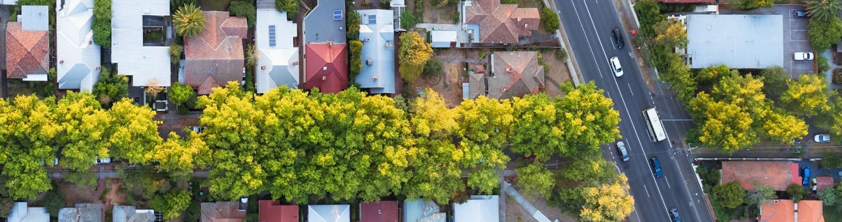 Aerial view of a suburban neighbourhood with houses, tree-lined streets and a main road running alongside the area