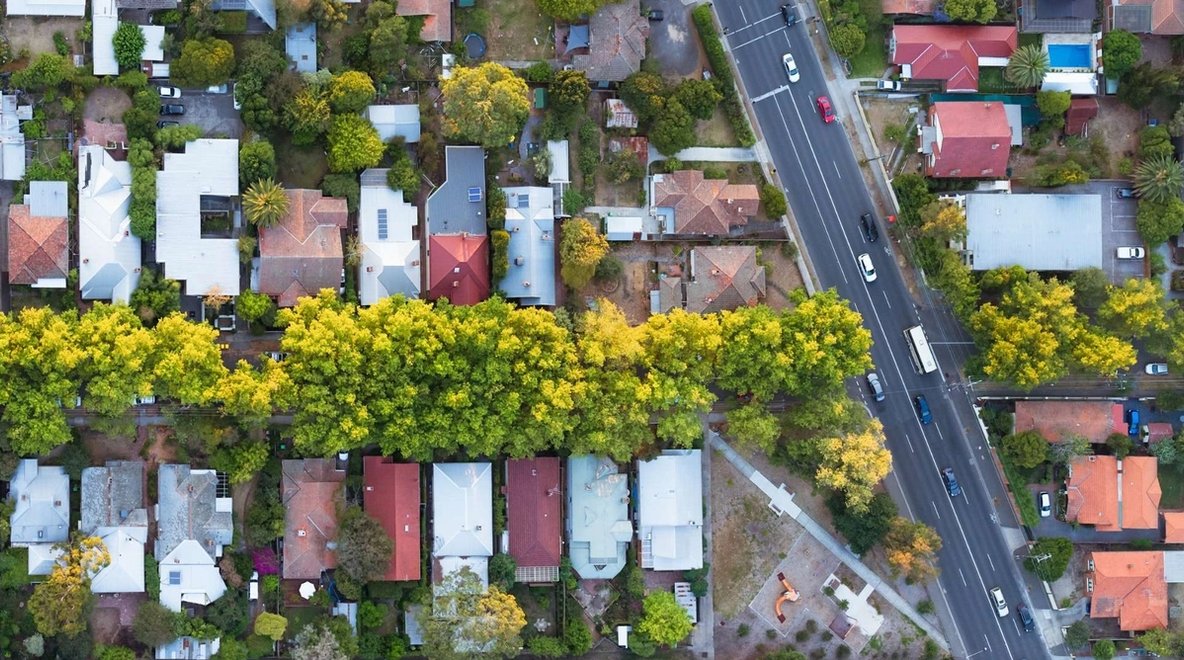 Aerial view of a suburban neighbourhood with houses, tree-lined streets and a main road running alongside the area