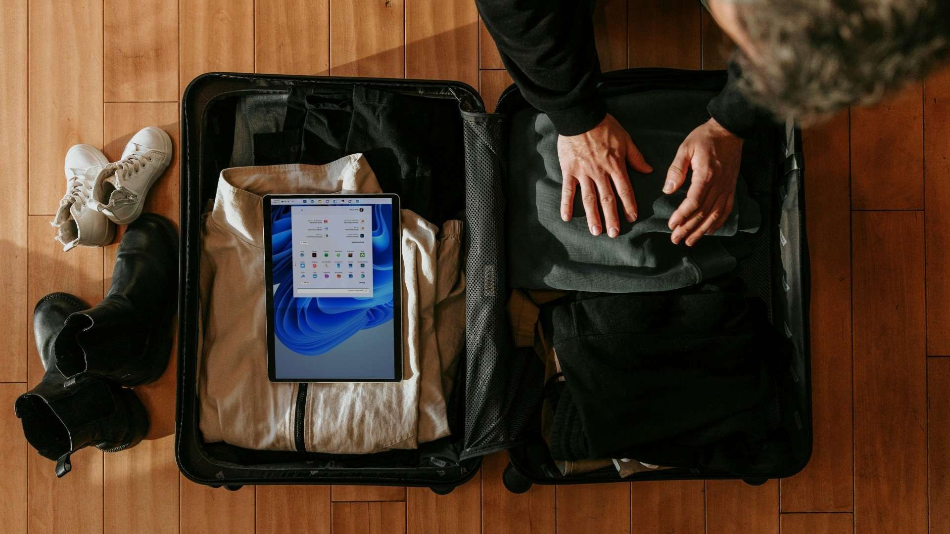Open suitcase on a wooden floor with clothes, shoes and a tablet packed beside a bag