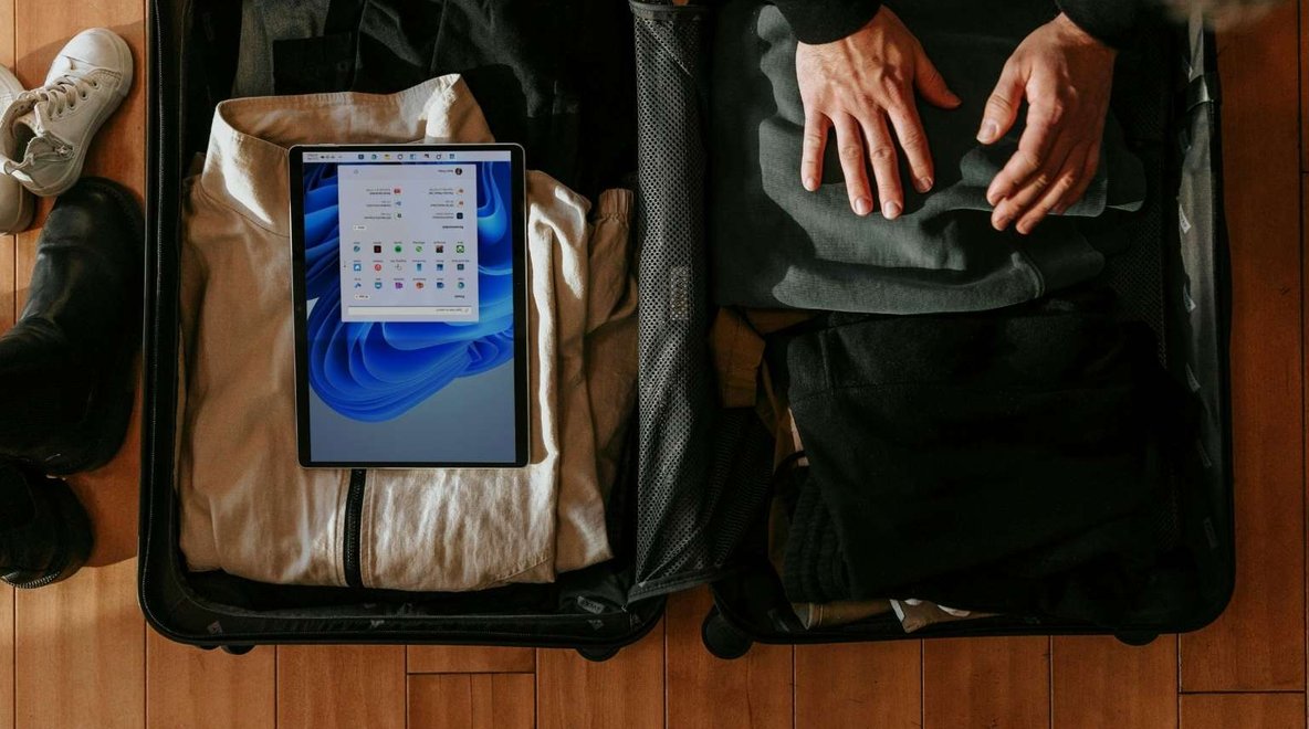 Open suitcase on a wooden floor with clothes, shoes and a tablet packed beside a bag