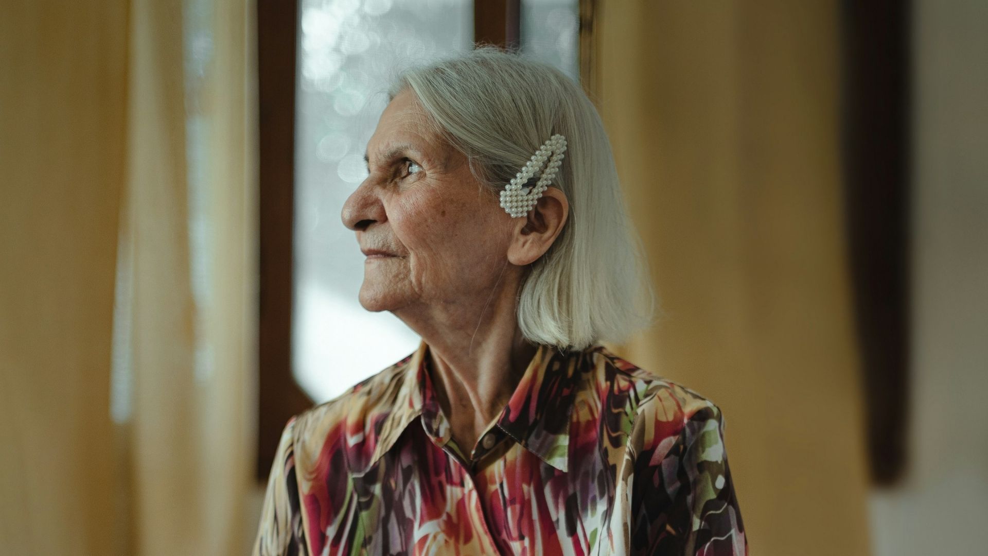 Older person looking out a window inside a home.