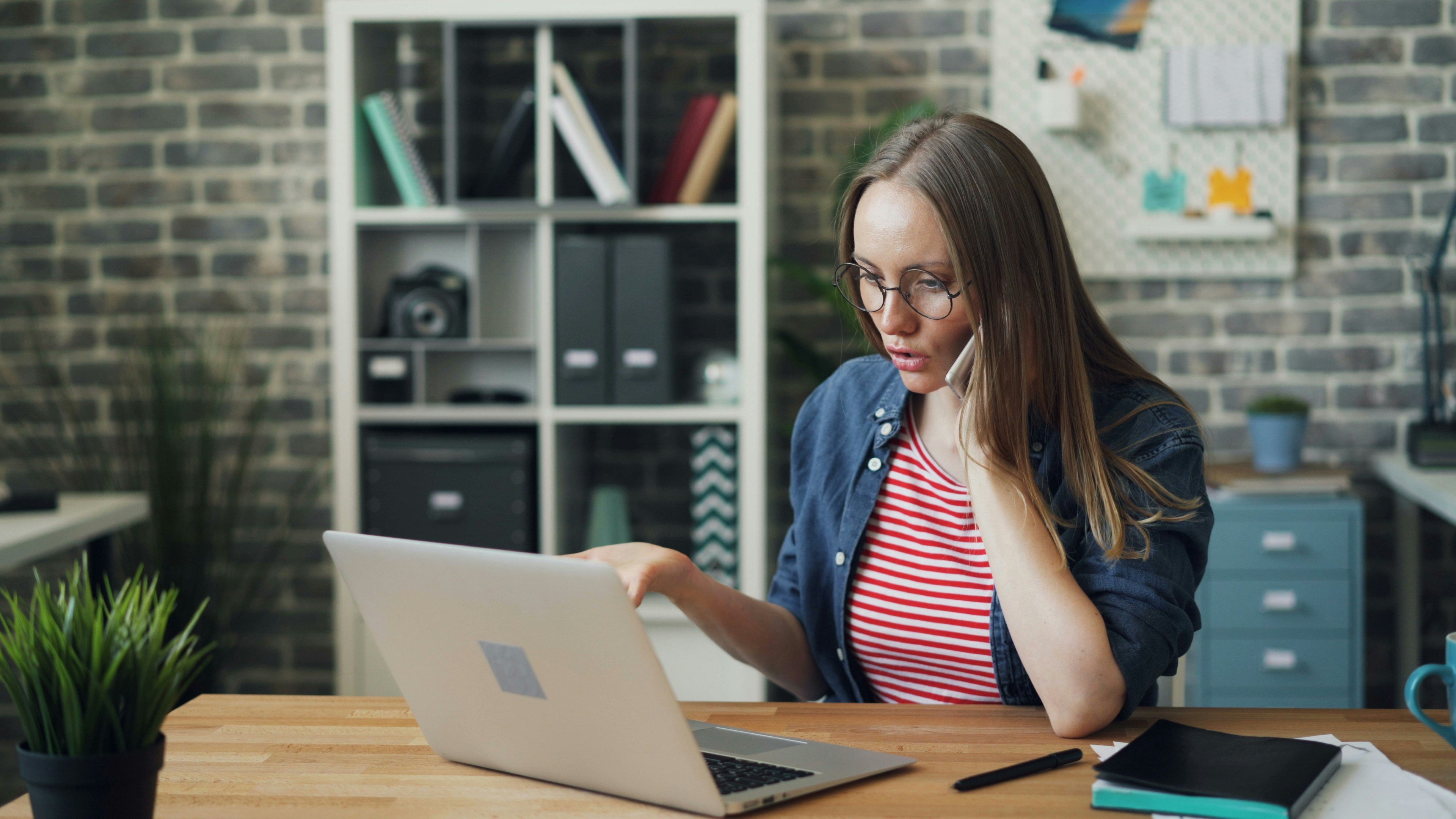 Person using a laptop at a desk while talking on the phone.