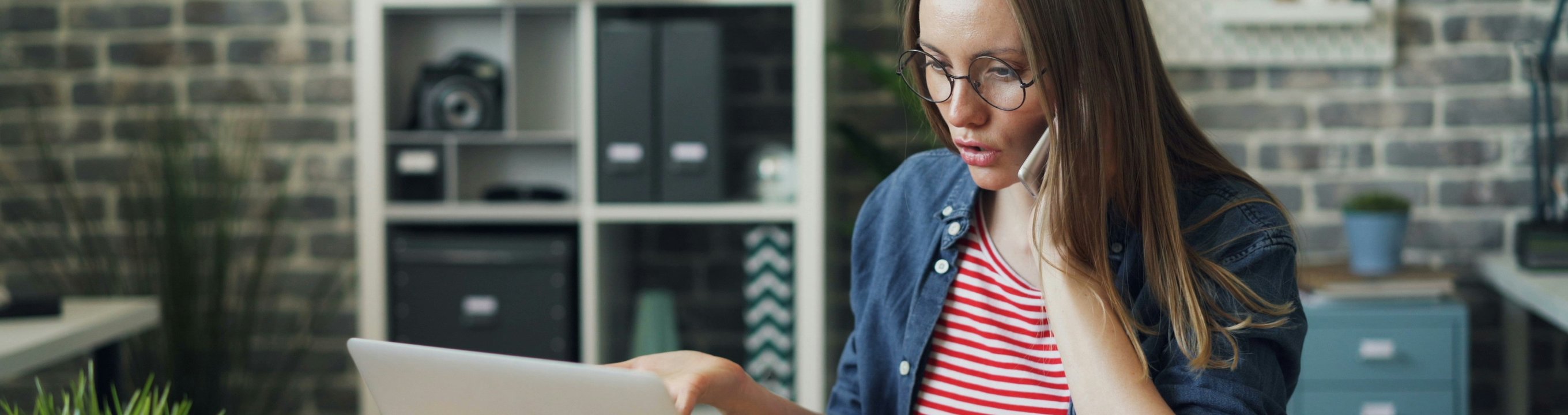 Person using a laptop at a desk while talking on the phone.