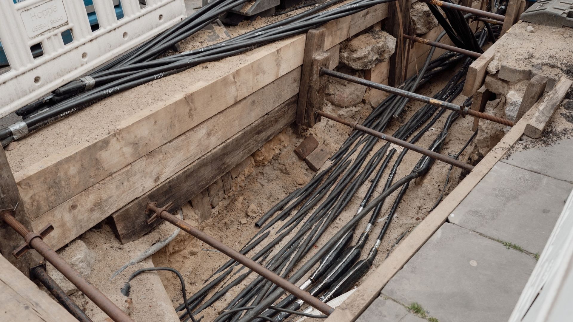 Excavated trench with multiple underground cables installed beneath a paved area.