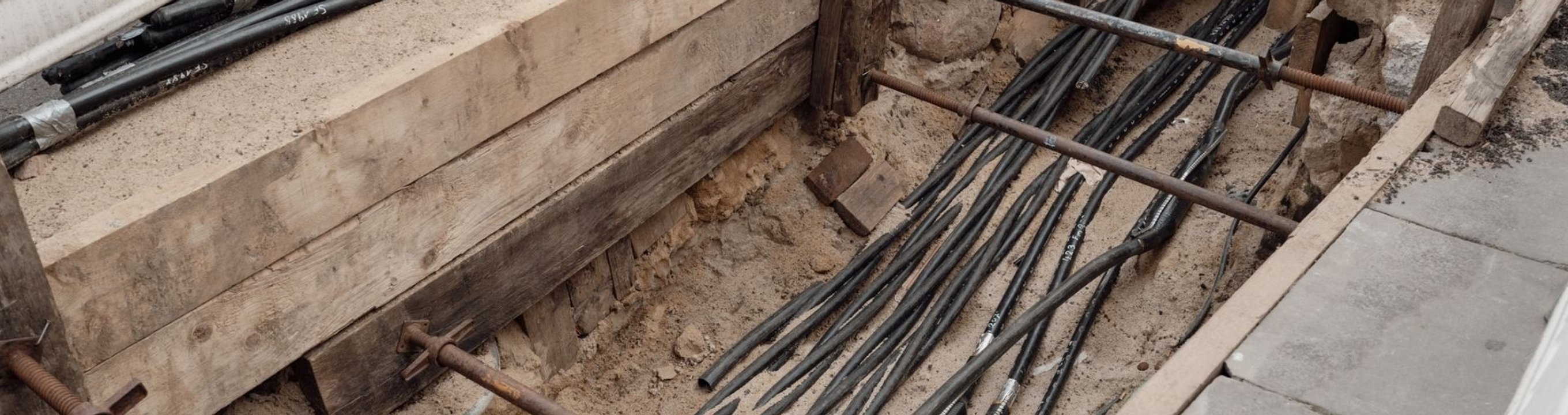 Excavated trench with multiple underground cables installed beneath a paved area.