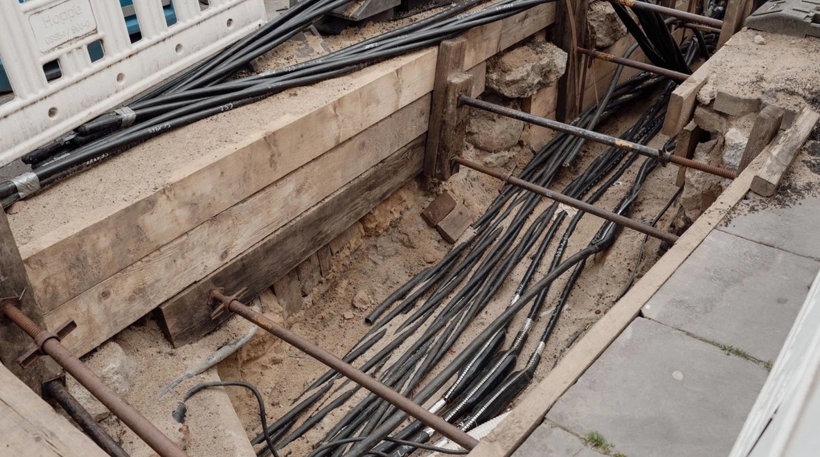 Excavated trench with multiple underground cables installed beneath a paved area.