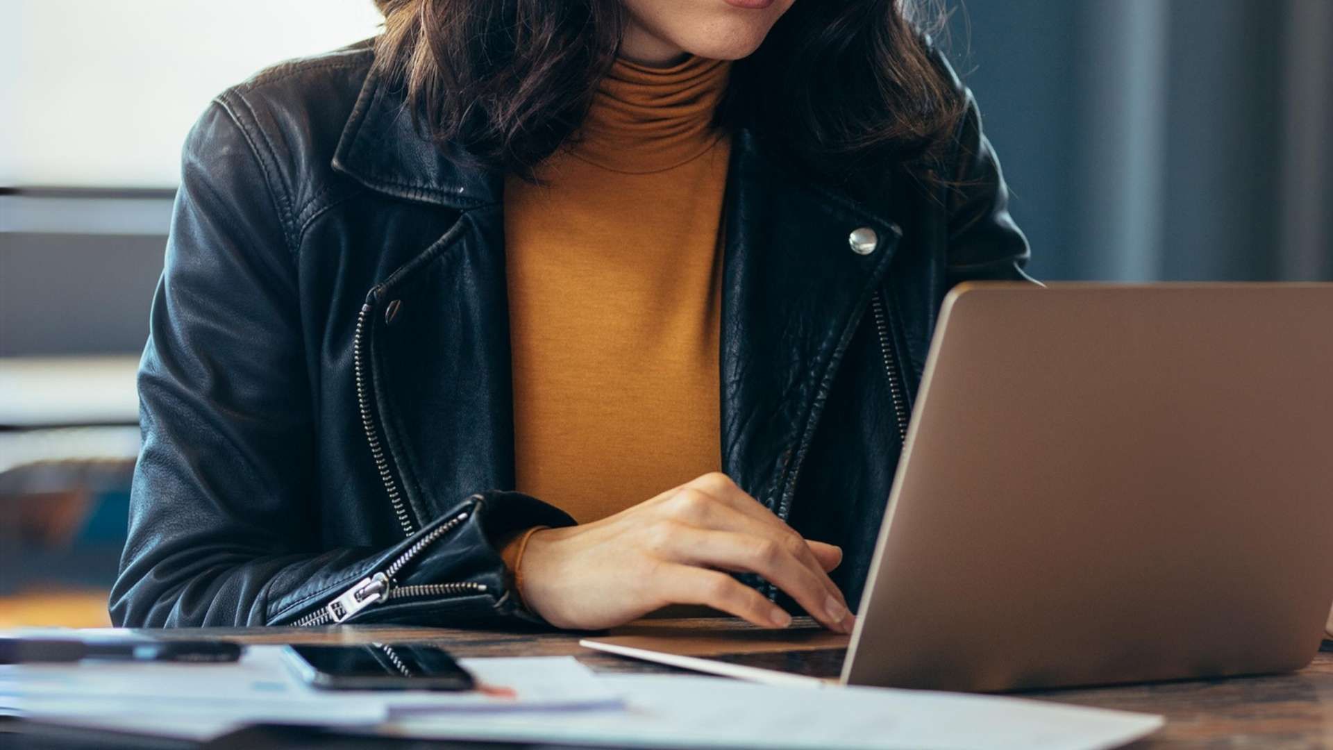Person using a laptop at a table with a smartphone and documents nearby