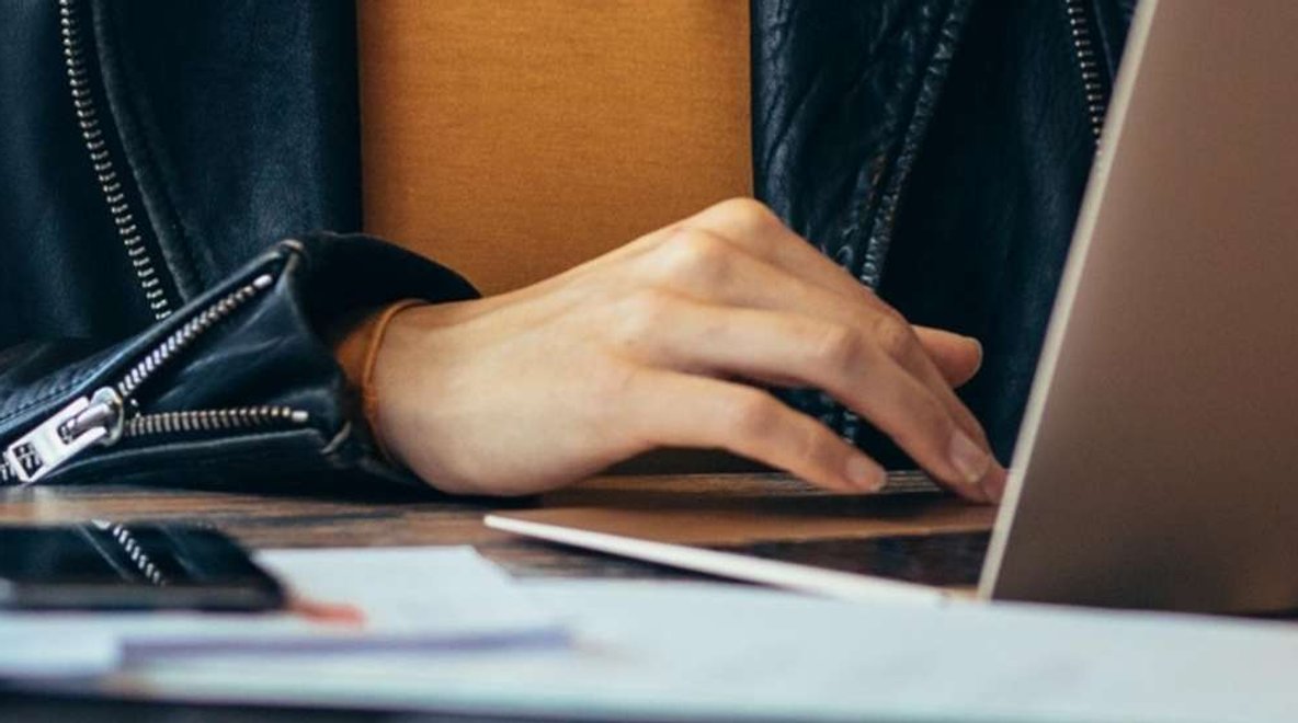 Person using a laptop at a table with a smartphone and documents nearby