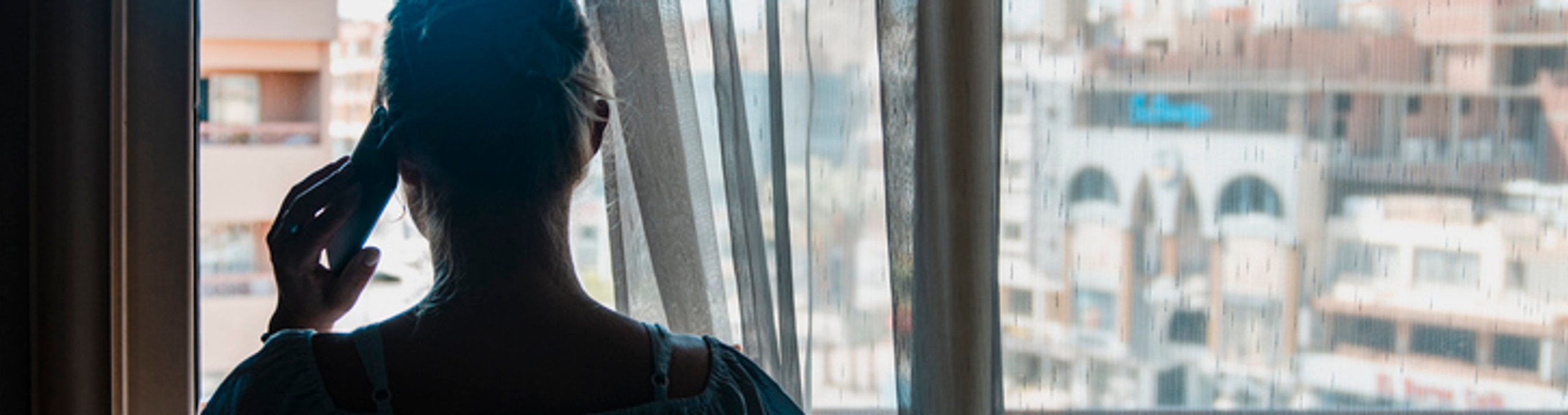 A person (woman) talking on a phone looking outside the window