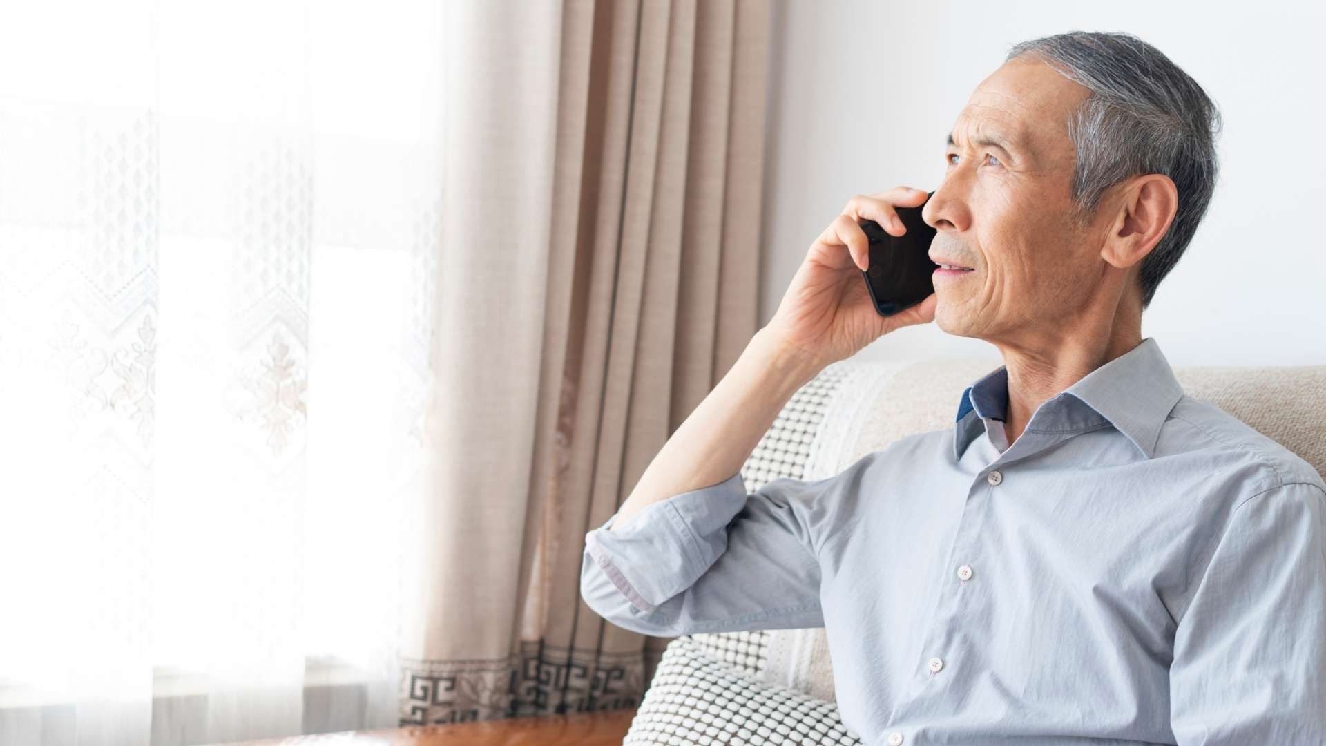 Person holding a mobile phone to ear while sitting beside a window.