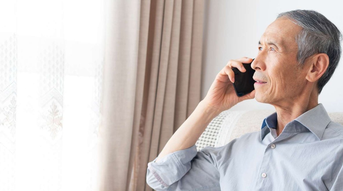 Person holding a mobile phone to ear while sitting beside a window.