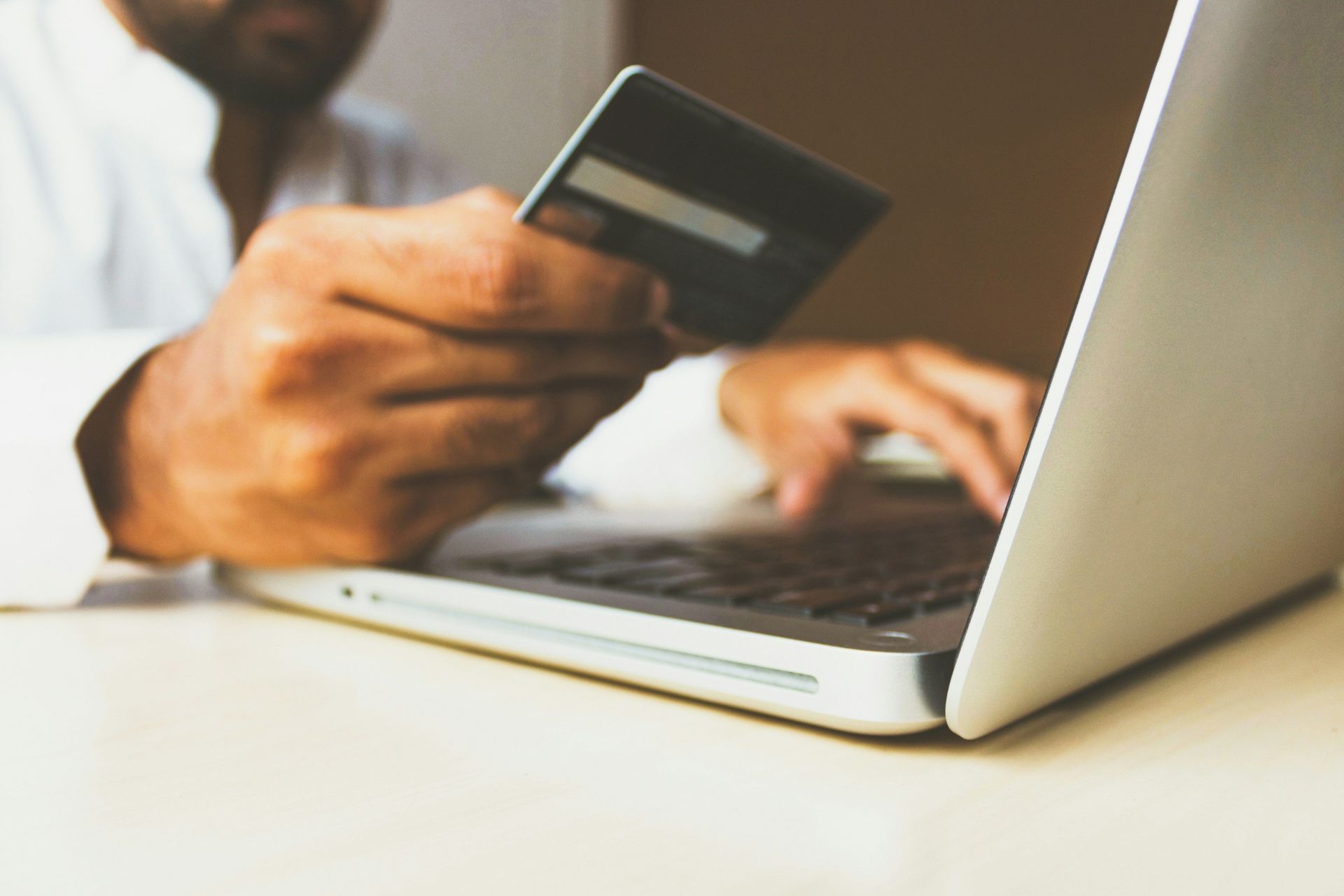Close-up of a person holding a credit card and using a laptop.