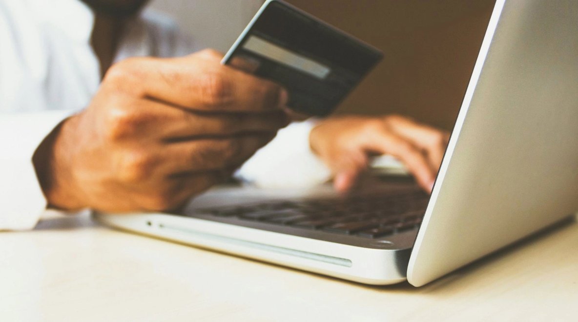 Close-up of a person holding a credit card and using a laptop.