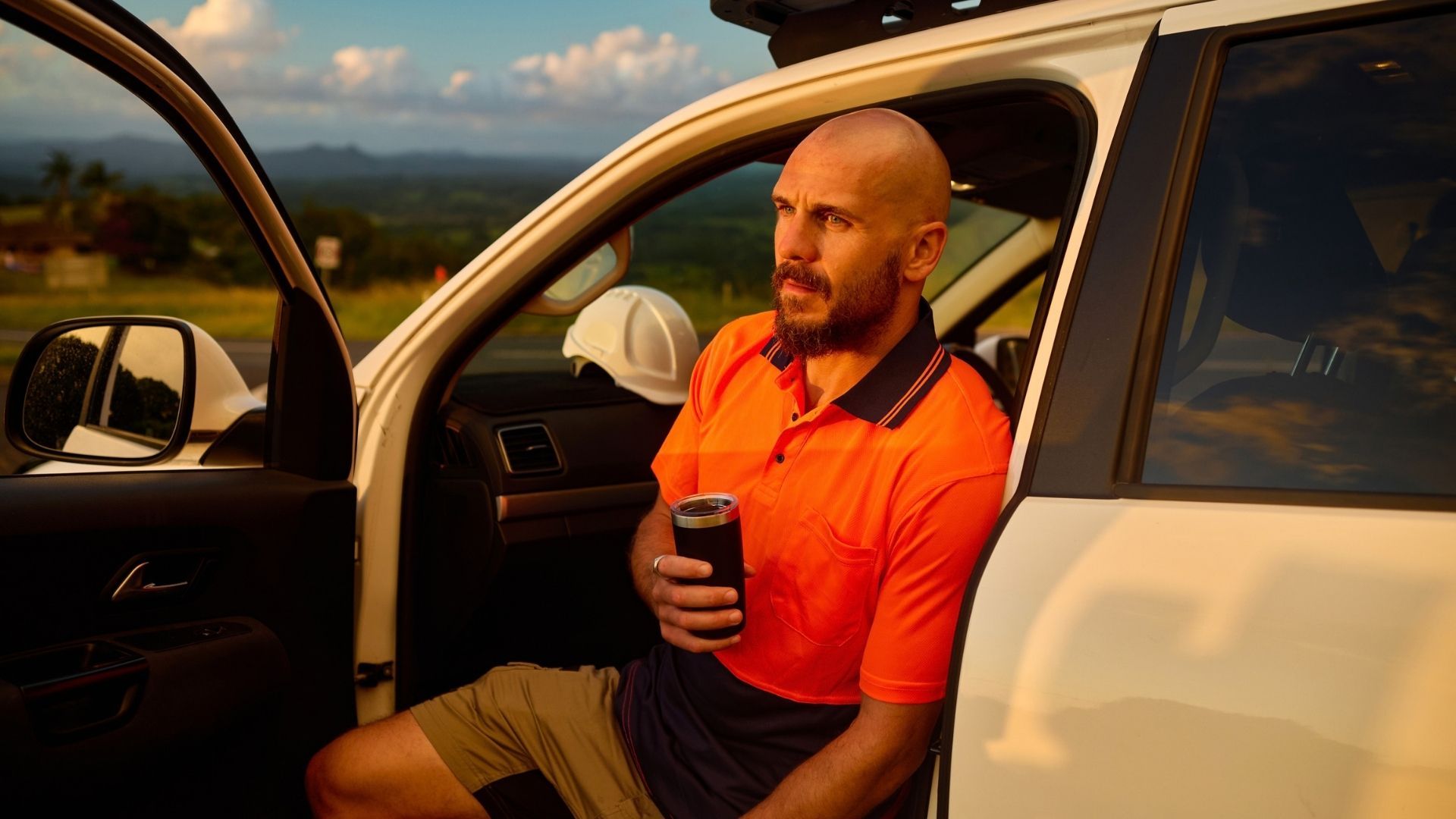 Person sitting in the open doorway of a utility vehicle with a rural landscape visible in the background.