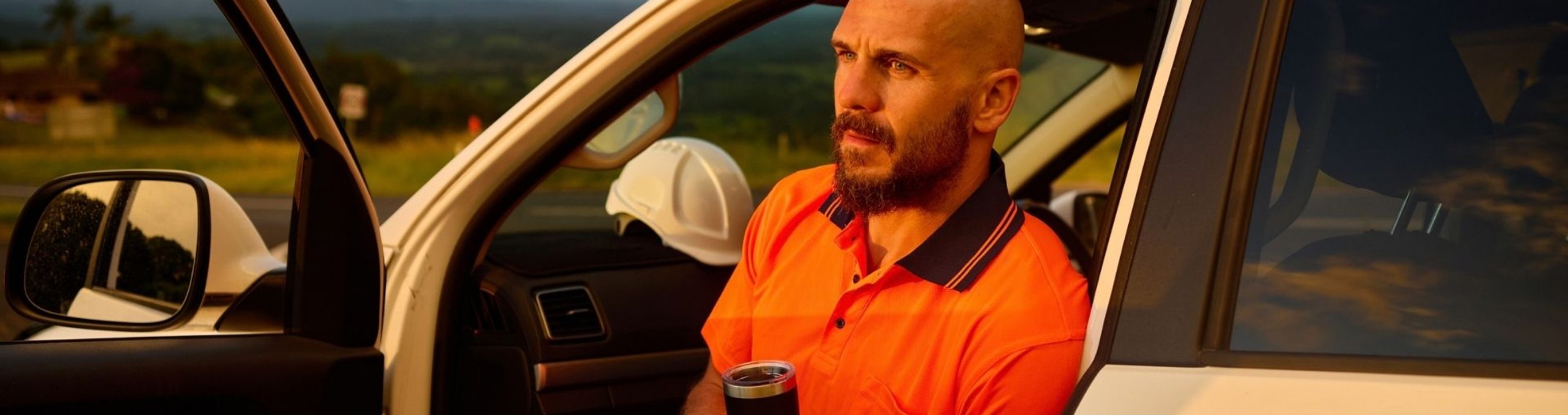 Person sitting in the open doorway of a utility vehicle with a rural landscape visible in the background.