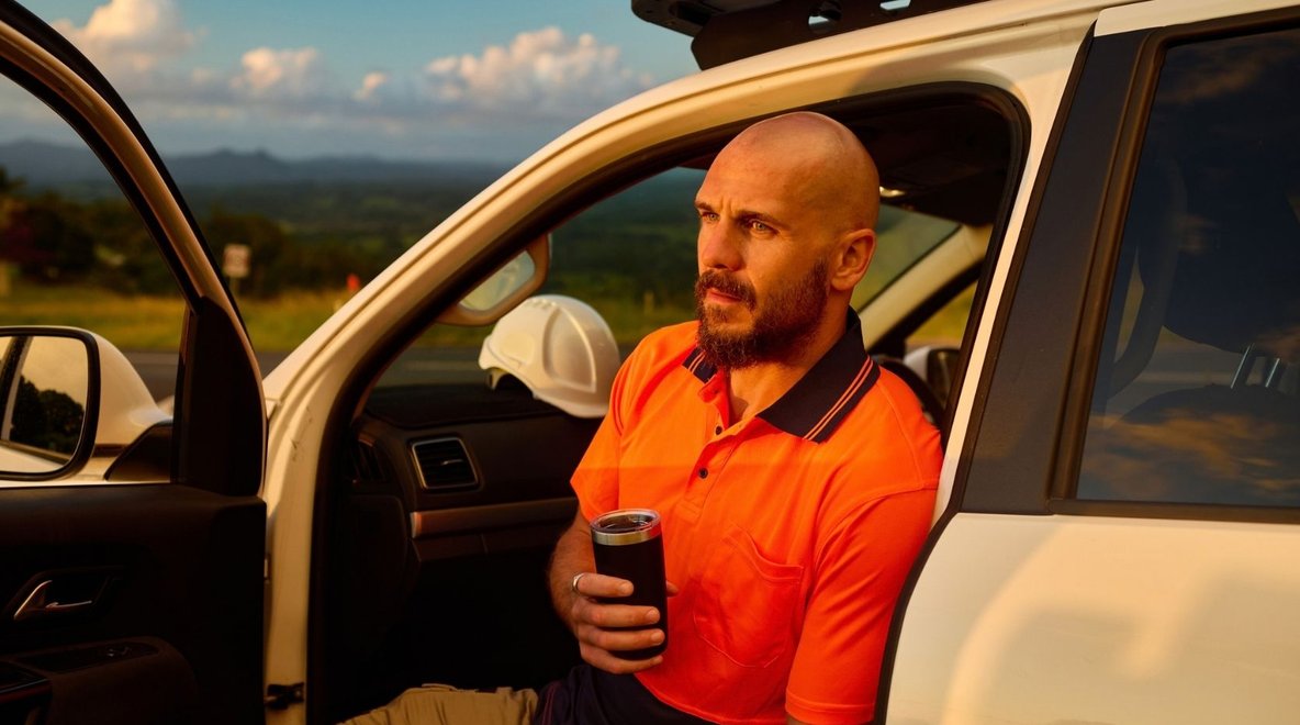 Person sitting in the open doorway of a utility vehicle with a rural landscape visible in the background.