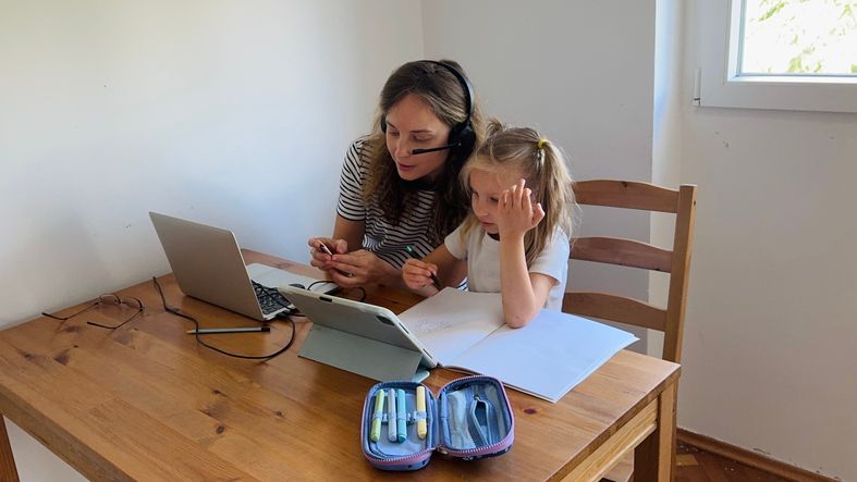 Two people sitting at a table using a laptop and writing in a notebook.
