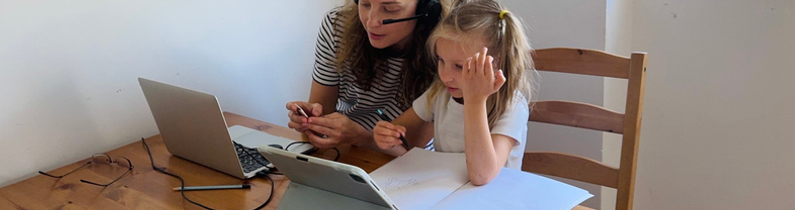 Two people sitting at a table using a laptop and writing in a notebook.