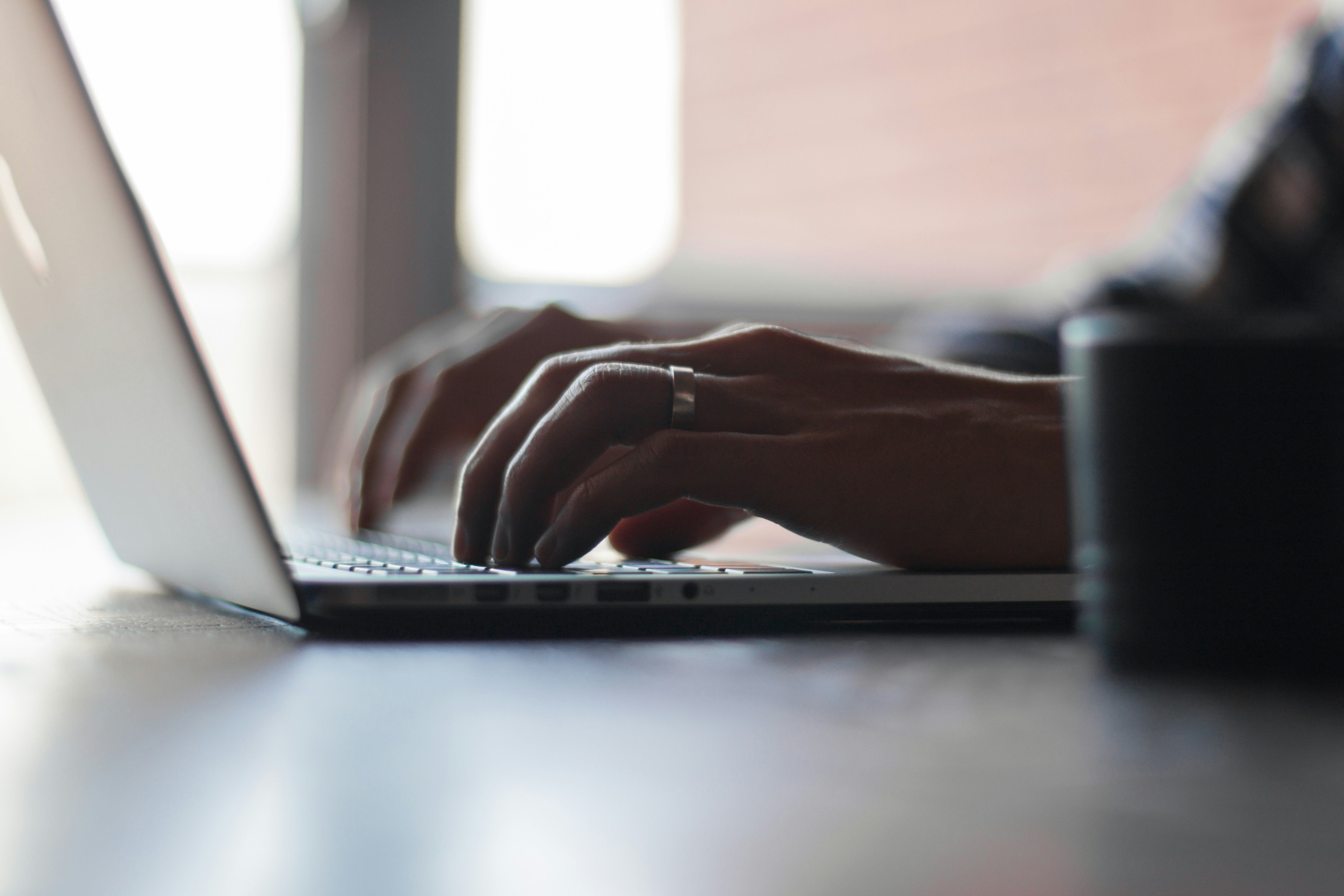 Close-up of hands typing on a laptop keyboard at a desk.