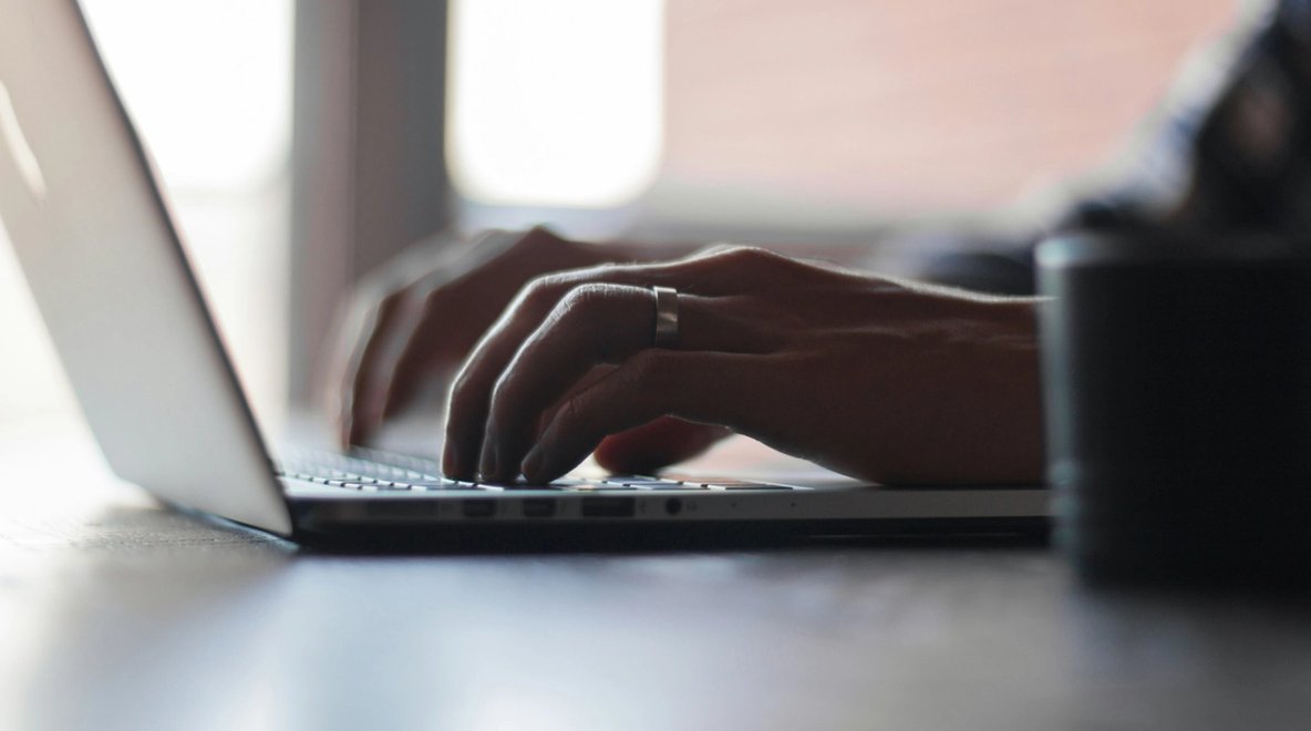 Close-up of hands typing on a laptop keyboard at a desk.