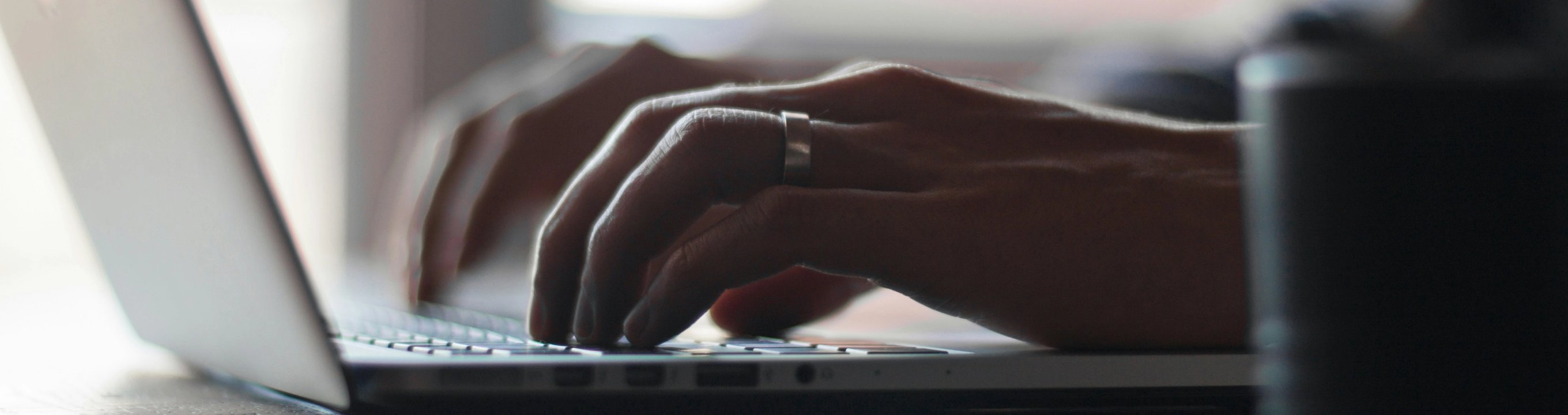Close-up of hands typing on a laptop keyboard at a desk.