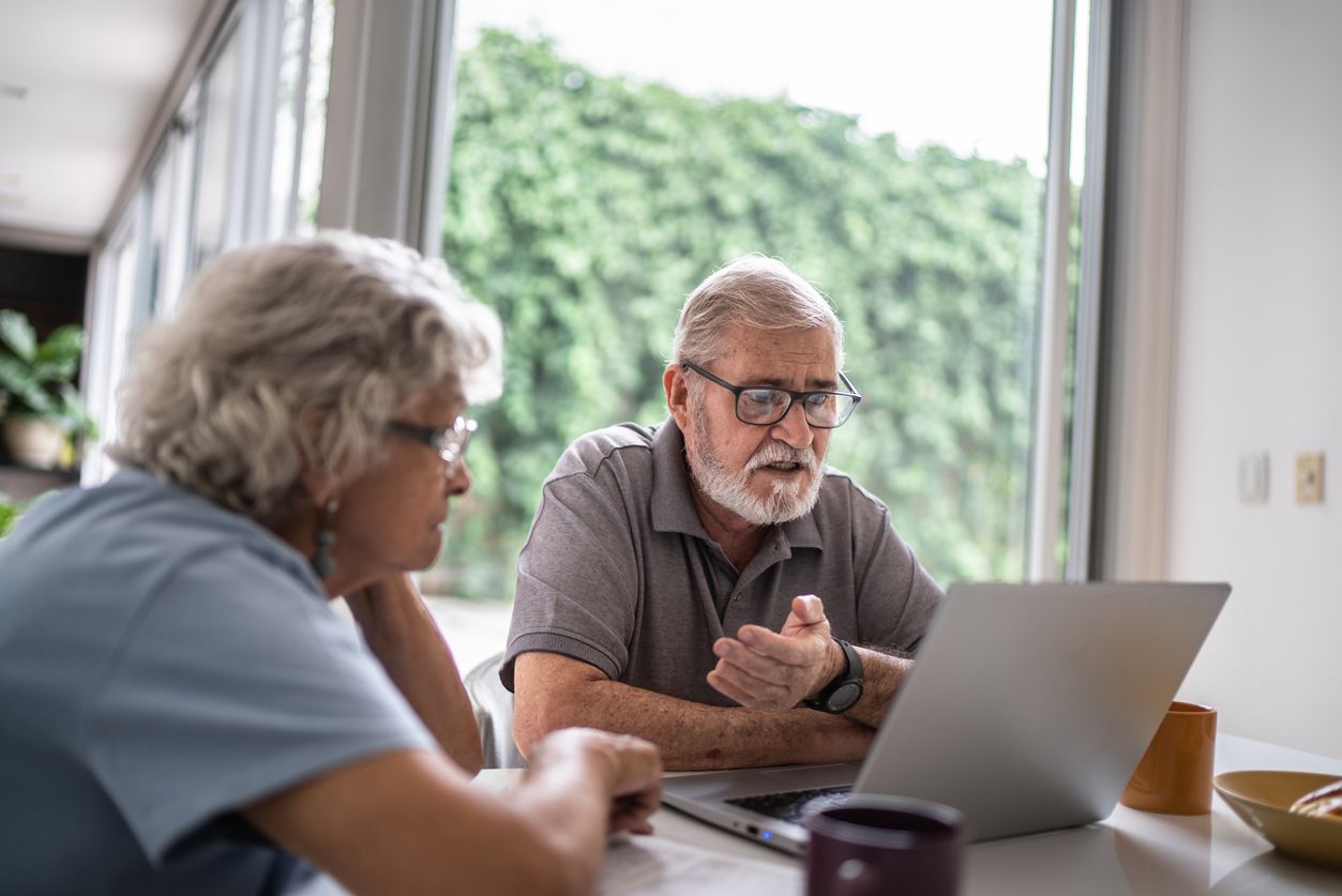 Two people sitting at a table looking at a laptop together near a window.