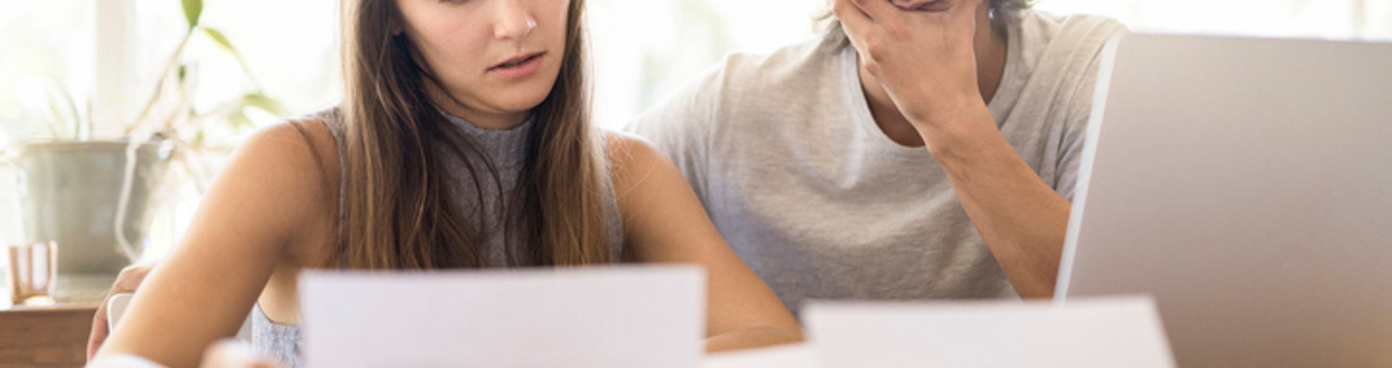Two people reviewing documents together at a table beside a laptop