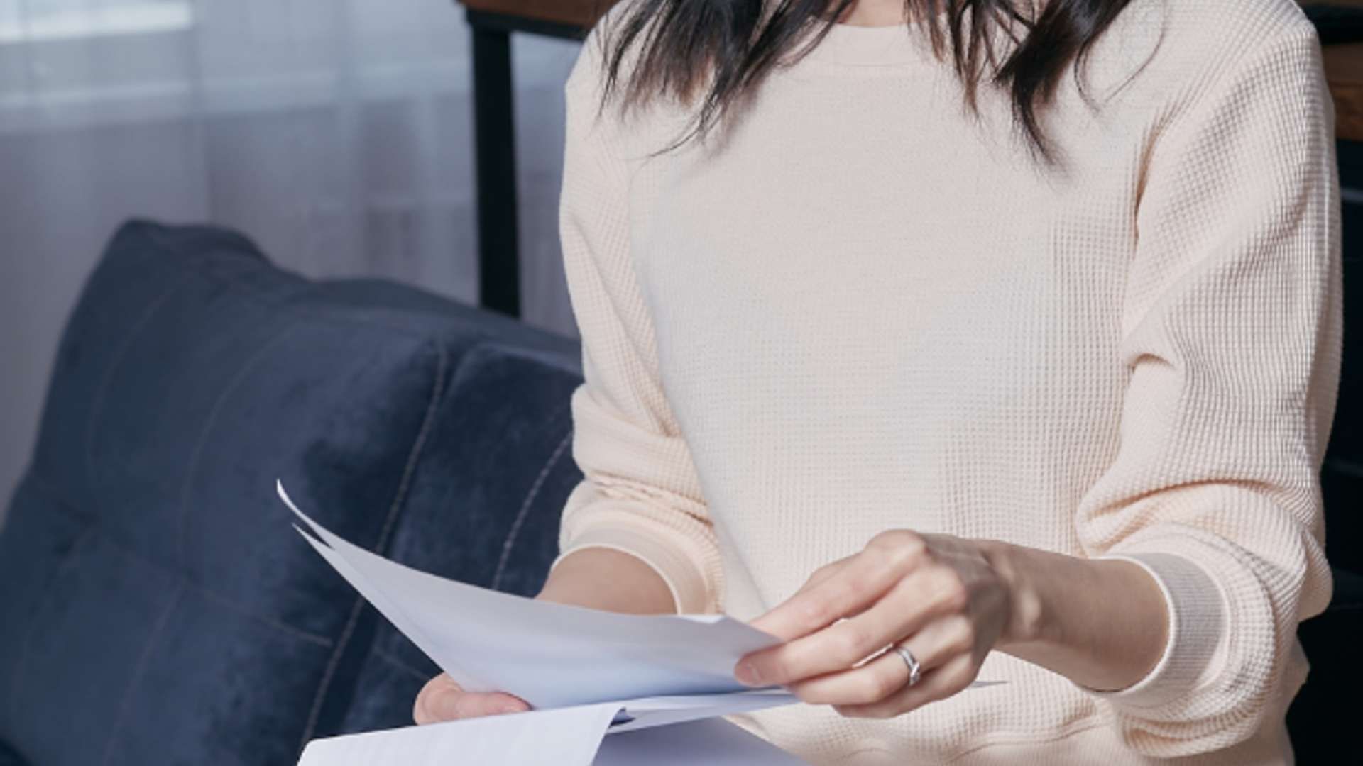 Person holding and reviewing bills while seated on a couch.