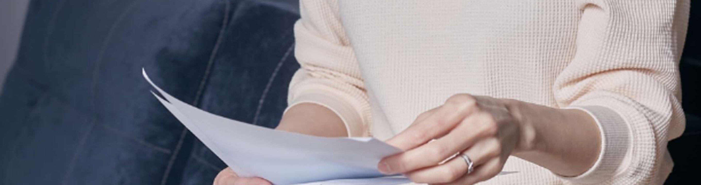Person holding and reviewing bills while seated on a couch.