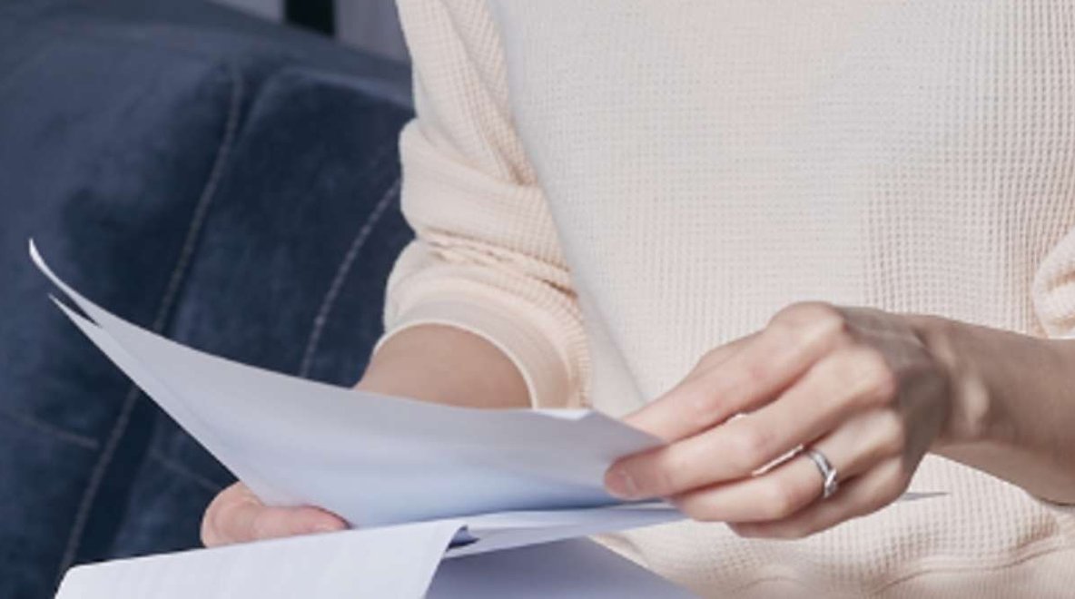 Person holding and reviewing bills while seated on a couch.