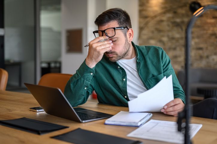 Person sitting at a desk holding a document and using a laptop.