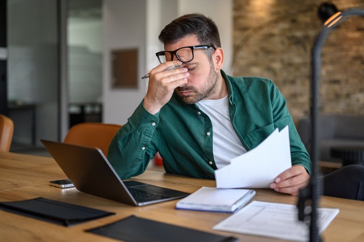 Person sitting at a desk holding a document and using a laptop.