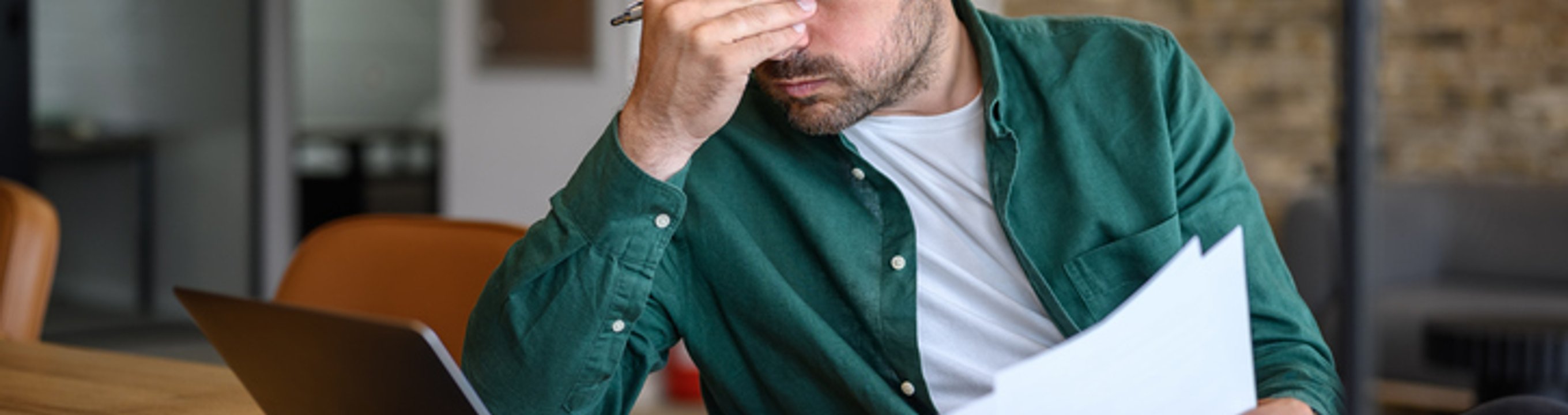 Person sitting at a desk holding a document and using a laptop.