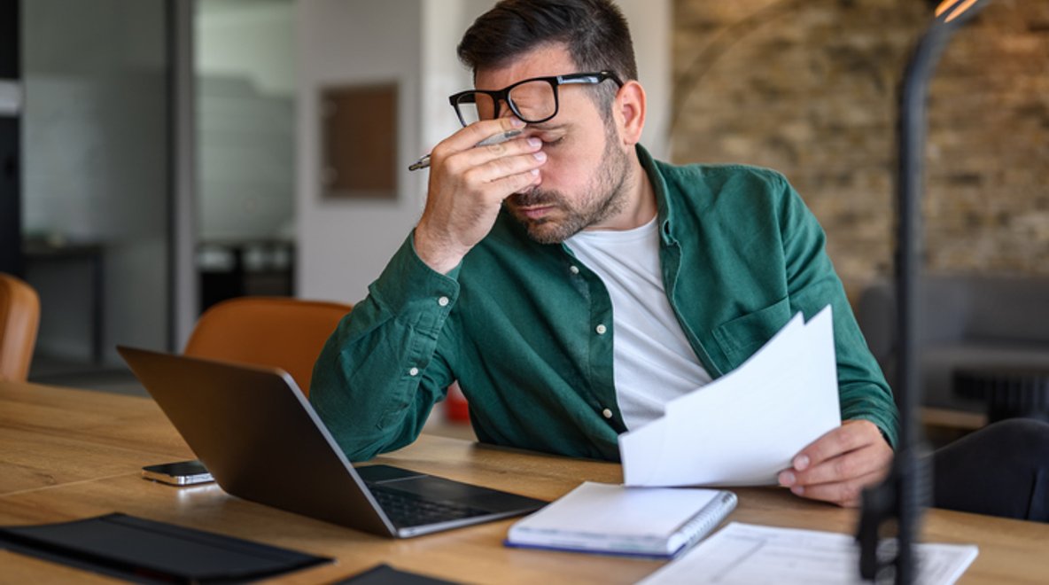 Person sitting at a desk holding a document and using a laptop.