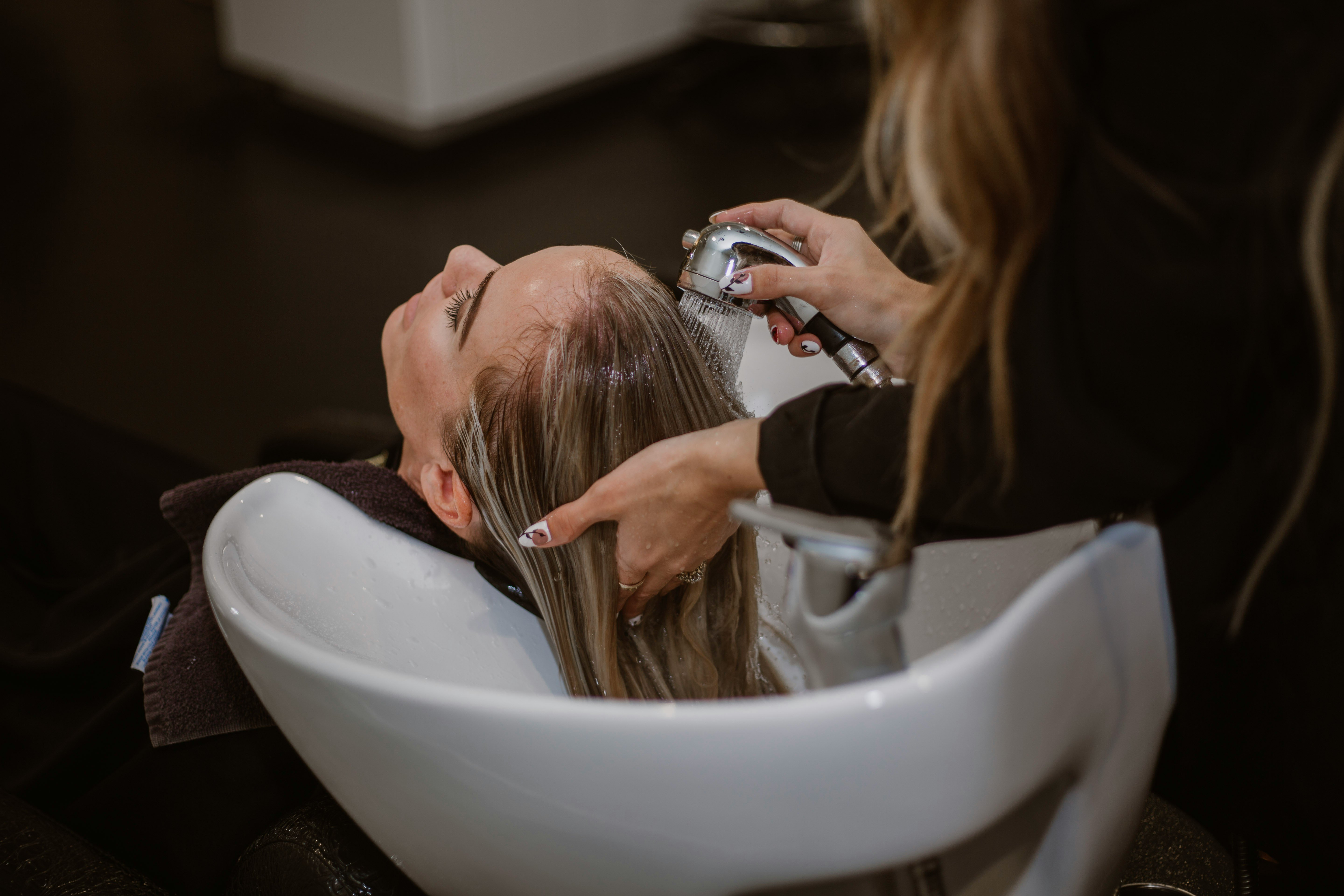 Close-up of a person washing someone’s hair at a salon sink.