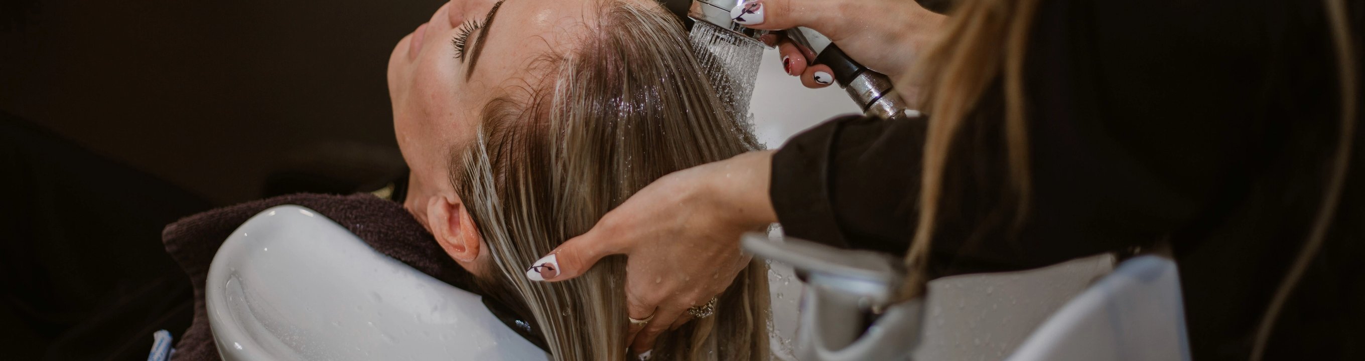 Close-up of a person washing someone’s hair at a salon sink.