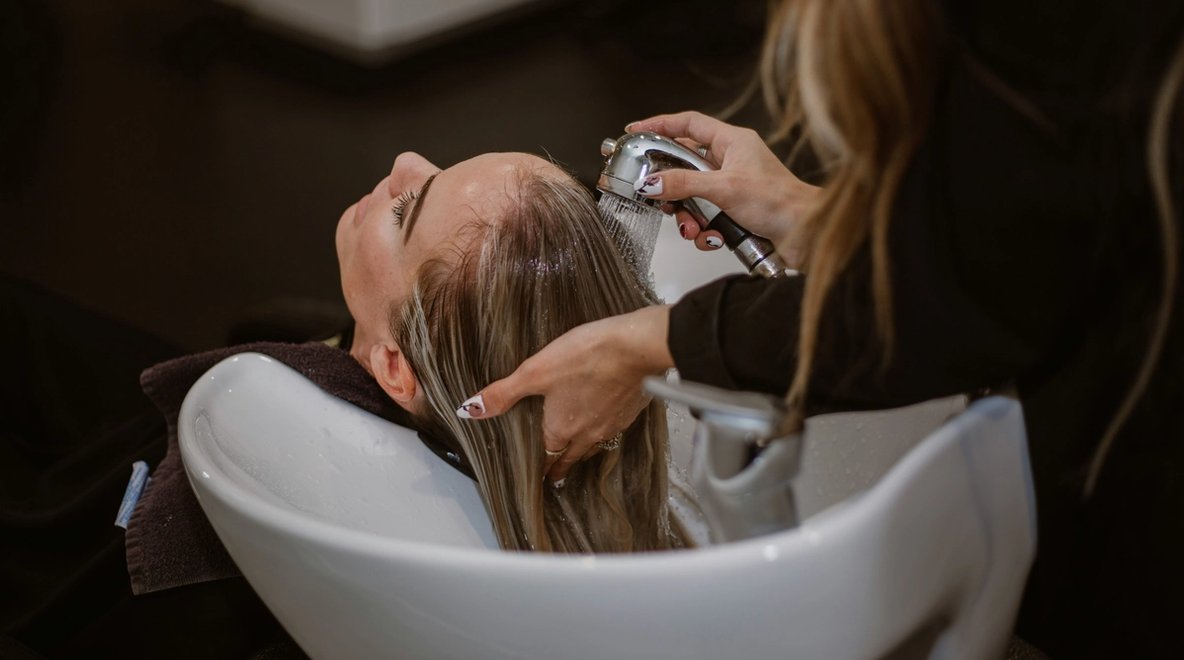 Close-up of a person washing someone’s hair at a salon sink.