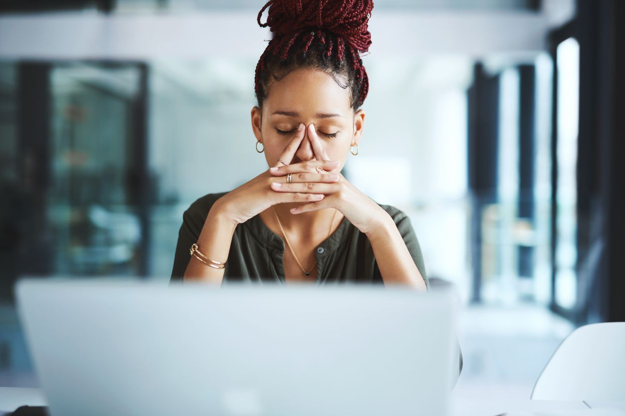 Person sitting at a desk with a laptop, hands clasped near face