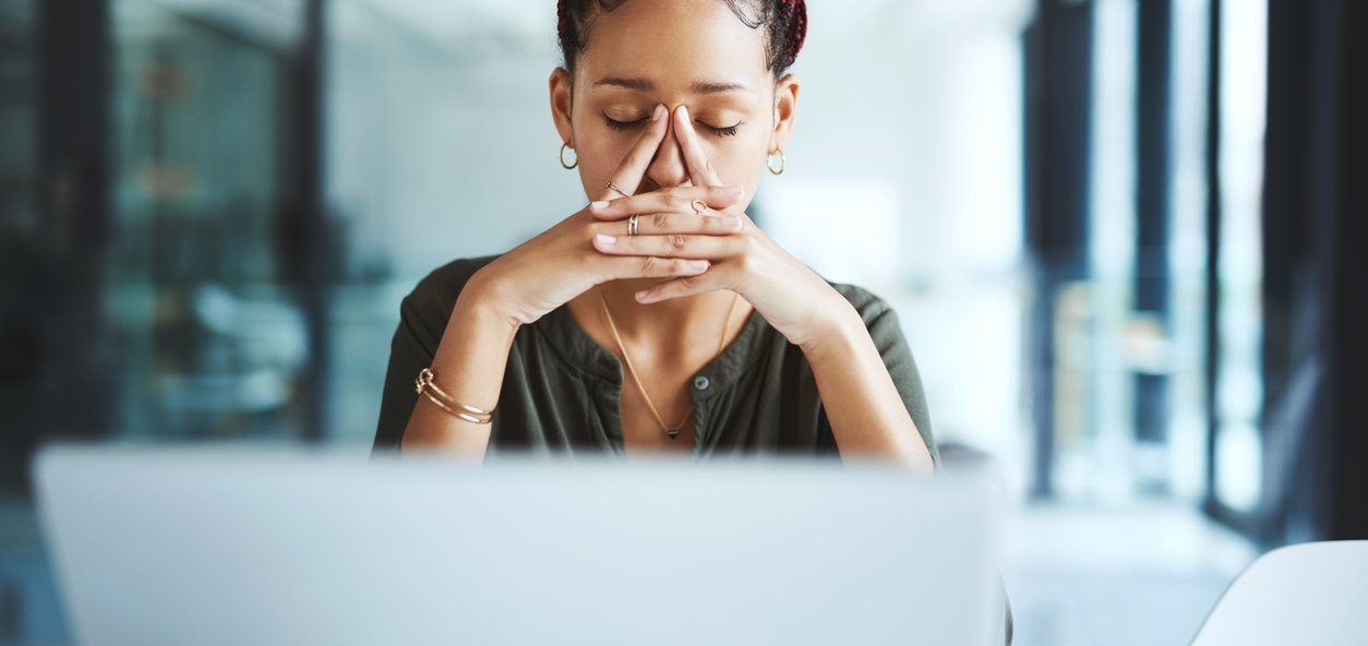 Person sitting at a desk with a laptop, hands clasped near face