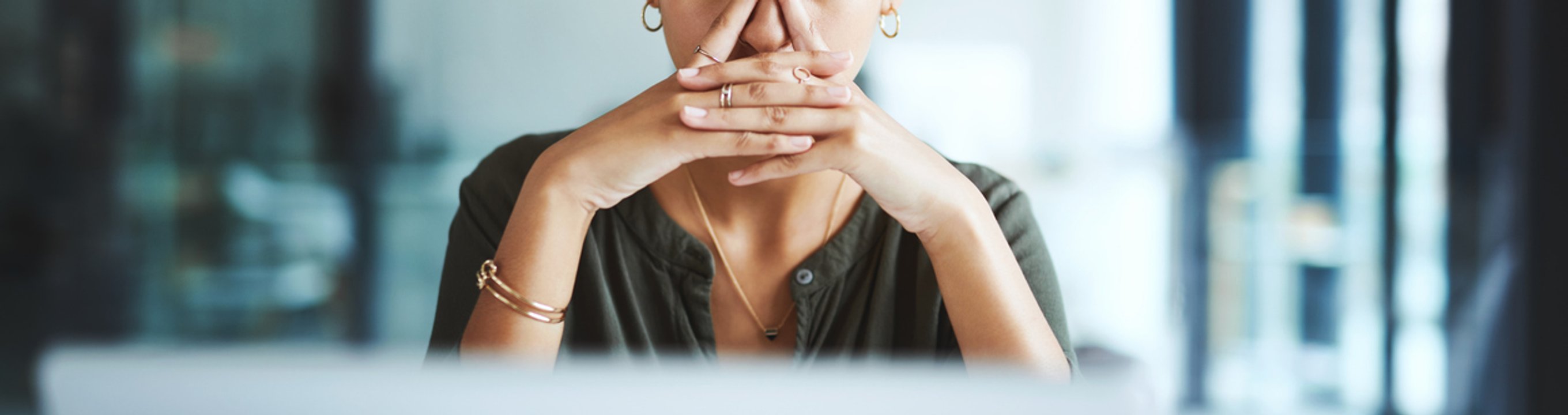 Person sitting at a desk with a laptop, hands clasped near face
